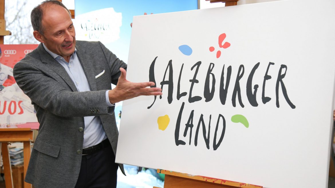Ein Mann im Anzug gestikuliert in Richtung eines Schildes mit der Aufschrift Salzburger Land und bunten Formen um den Text herum.