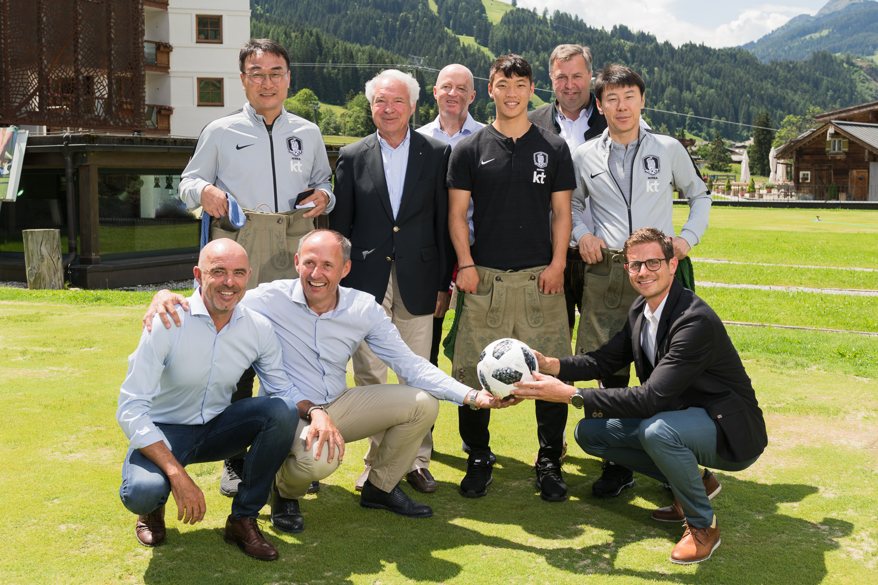 Eine Gruppe von Männern im Freien auf einer Wiese lächelt in die Kamera, zwei von ihnen halten einen Fußball in der Hand.