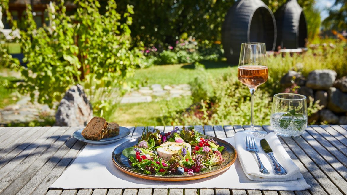 Ein frischer Salat, Brot, Roséwein und Wasser warten auf einem sonnenbeschienenen Gartentisch der Via Culinaria.