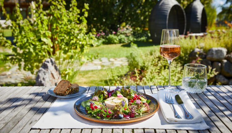 Ein frischer Salat, Brot, Roséwein und Wasser warten auf einem sonnenbeschienenen Gartentisch der Via Culinaria.