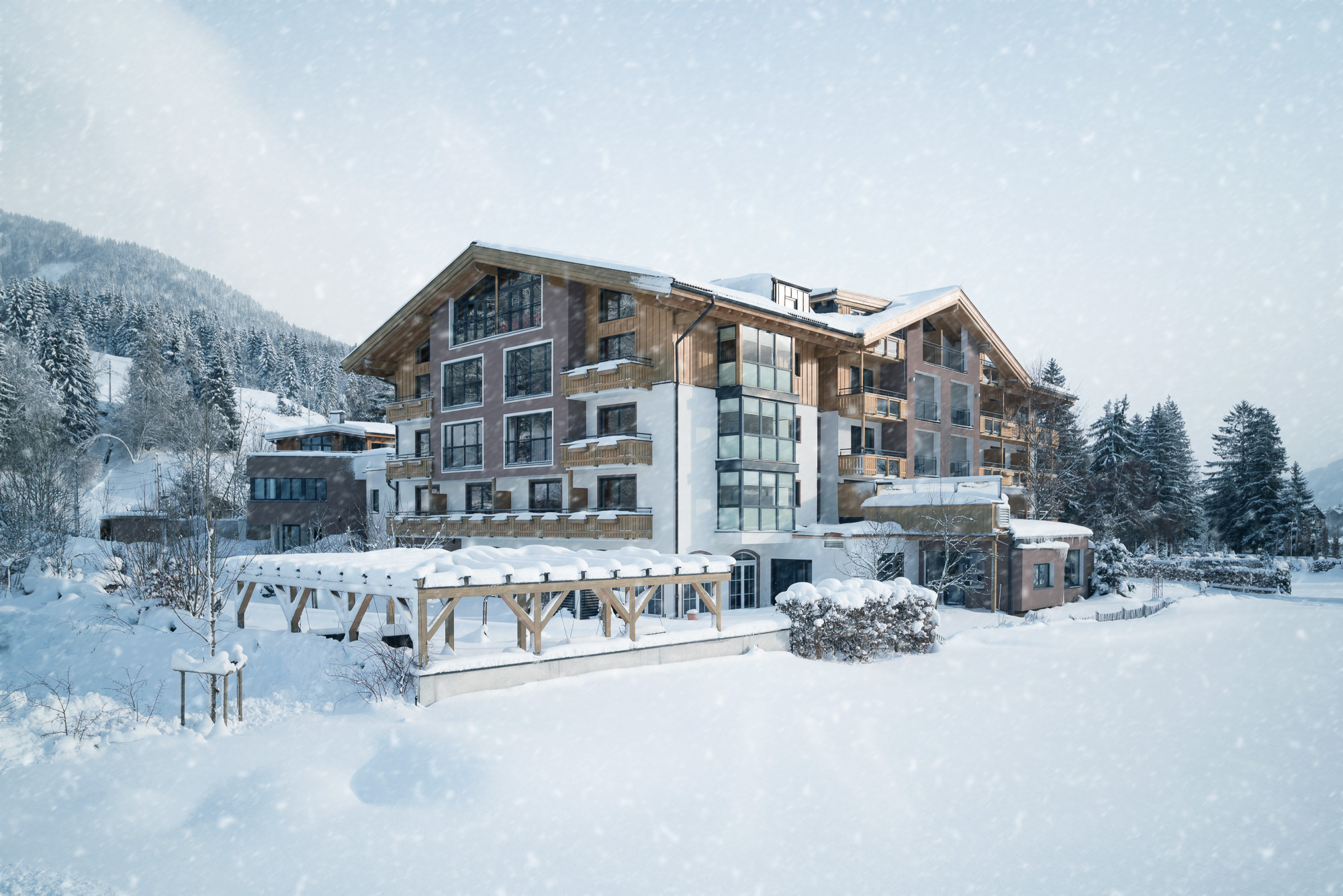 Ein großes österreichisches Hotel im Chalet-Stil, umgeben von schneebedeckten Bäumen und Bergen bei Schneefall.
