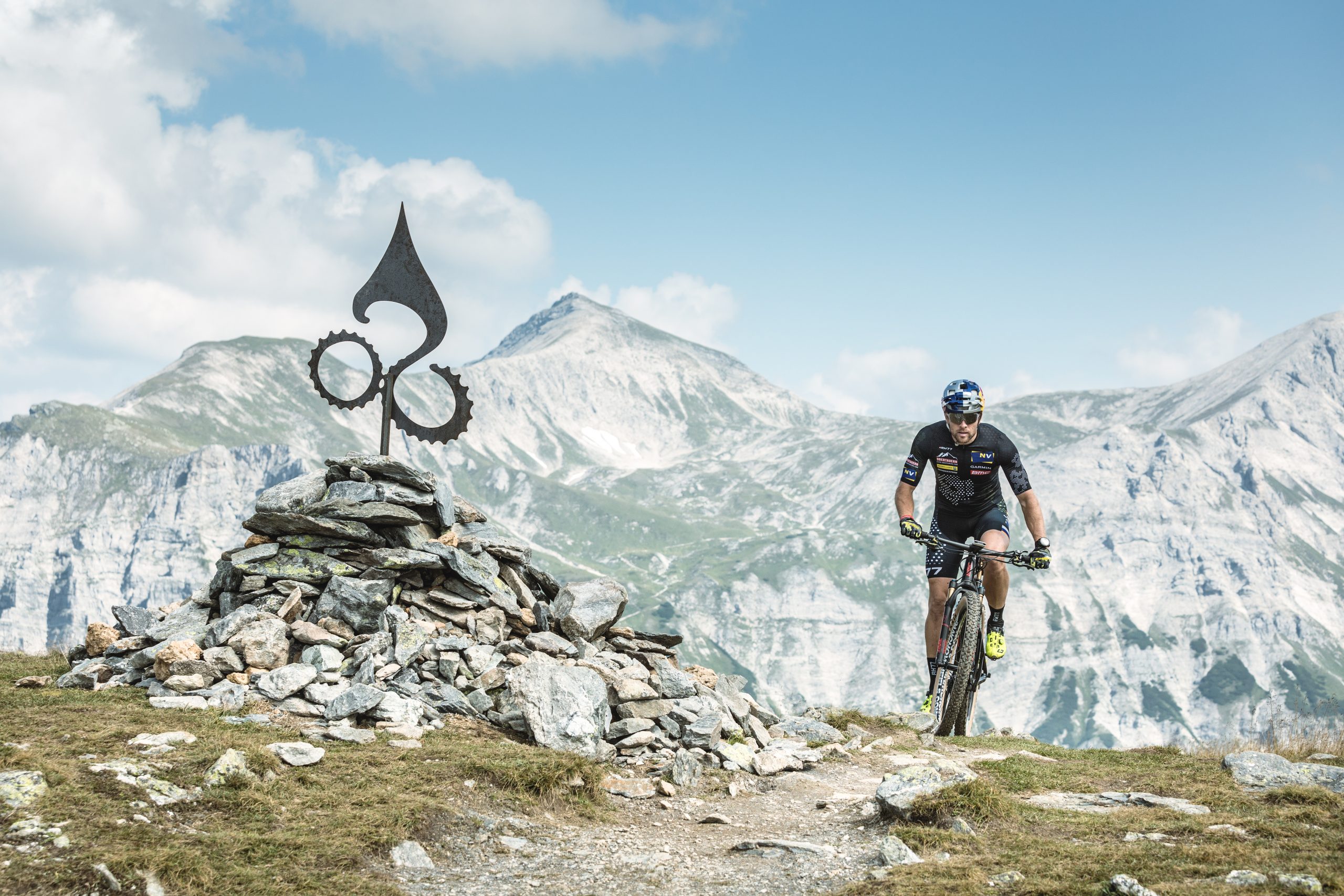 Ein Radfahrer fährt mit seinem Mountainbike auf einem felsigen Weg in der Nähe eines Steinhaufens mit Bergen im Hintergrund.