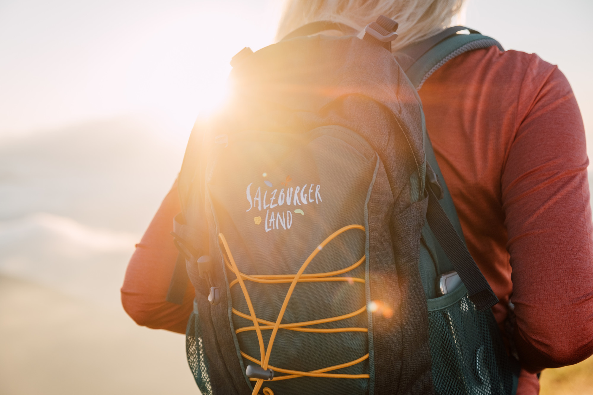 Person mit einem Salzburger Land-Rucksack im Freien, im Hintergrund scheint das Sonnenlicht.