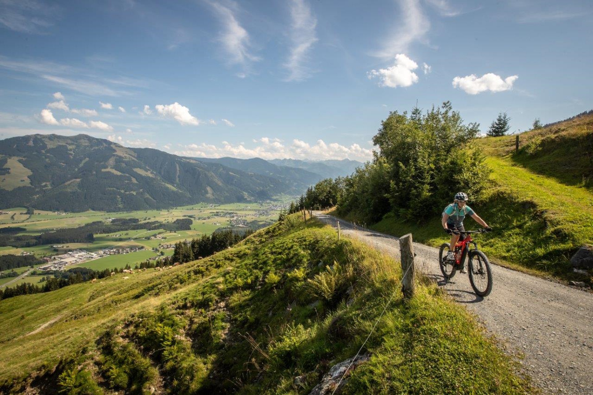 Eine Person fährt mit dem Mountainbike auf einem Weg mit Blick auf ein malerisches Tal mit Bergen im Hintergrund.