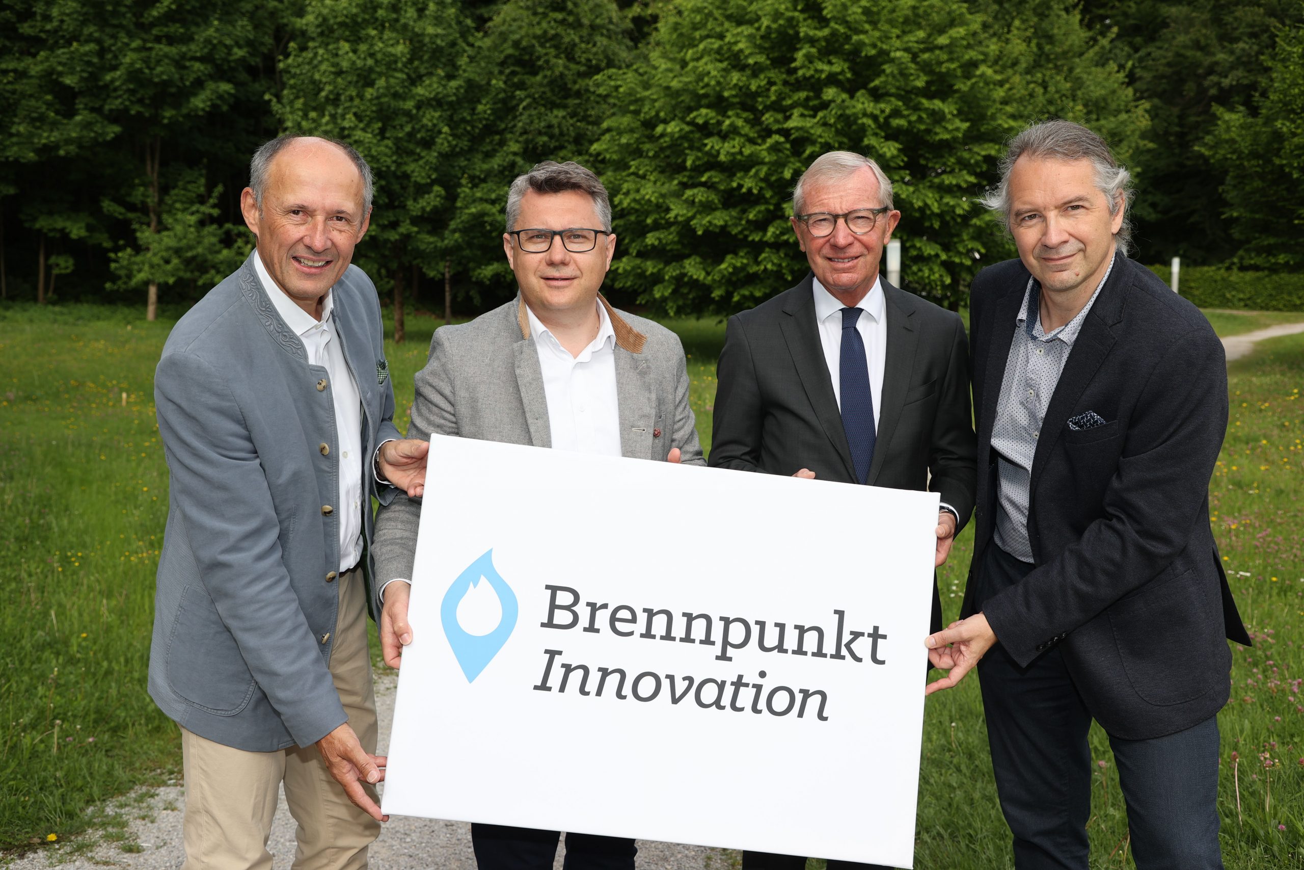 Vier Männer stehen im Freien und halten ein Schild mit der Aufschrift Brennpunkt Innovation und einem blauen Flammenlogo.