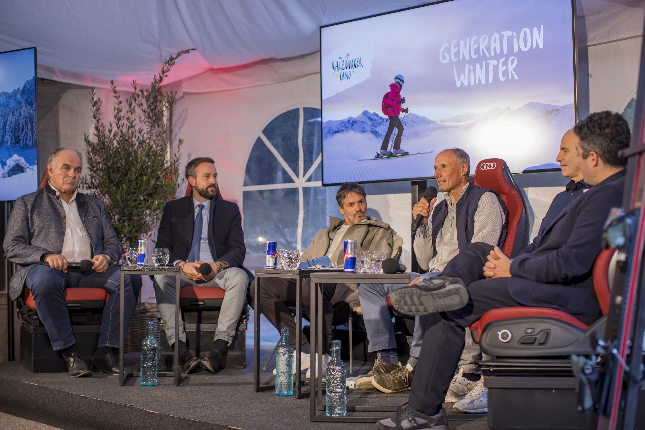 Sechs Männer sitzen auf der Bühne und führen eine Podiumsdiskussion vor zwei Bildschirmen, auf denen "Generation Winter" zu lesen ist.