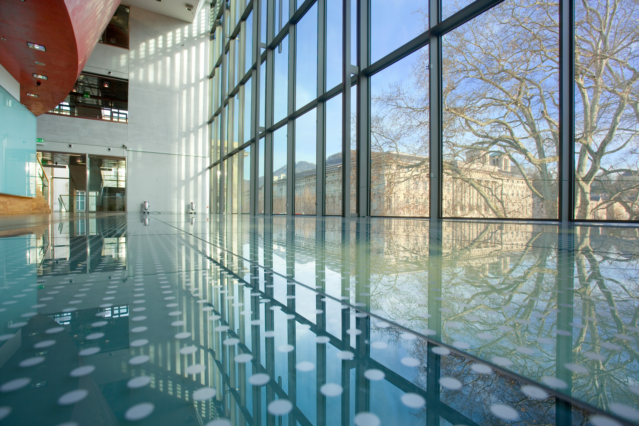 Modernes Gebäude mit Glaswänden und Spiegelungen von Bäumen und Himmel auf dem polierten Boden.