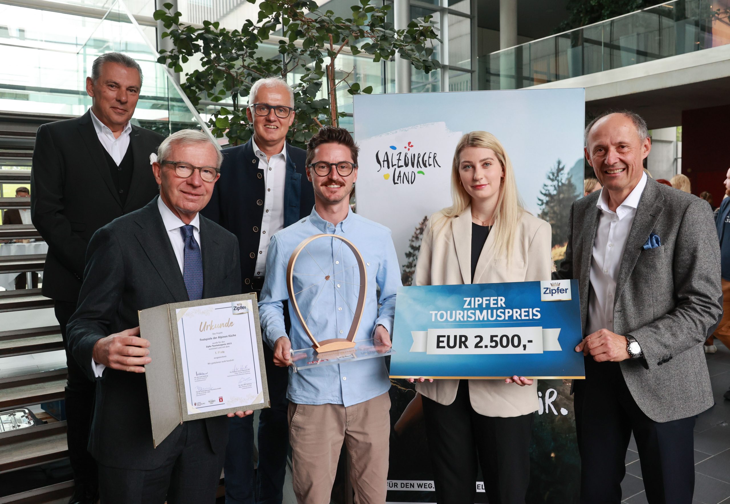Sechs Personen posieren mit einer Urkunde, einer Trophäe und einem großen Scheck über 2 500 € für den Tourismuspreis in der Halle.