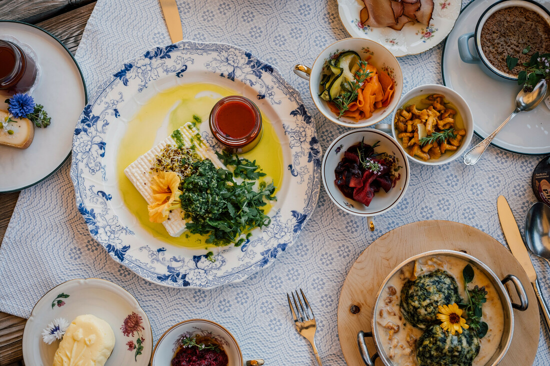 Ein Tisch mit verschiedenen bunten Gerichten, darunter Salate, Grünzeug, Soßen und Brot auf eleganten Tellern.