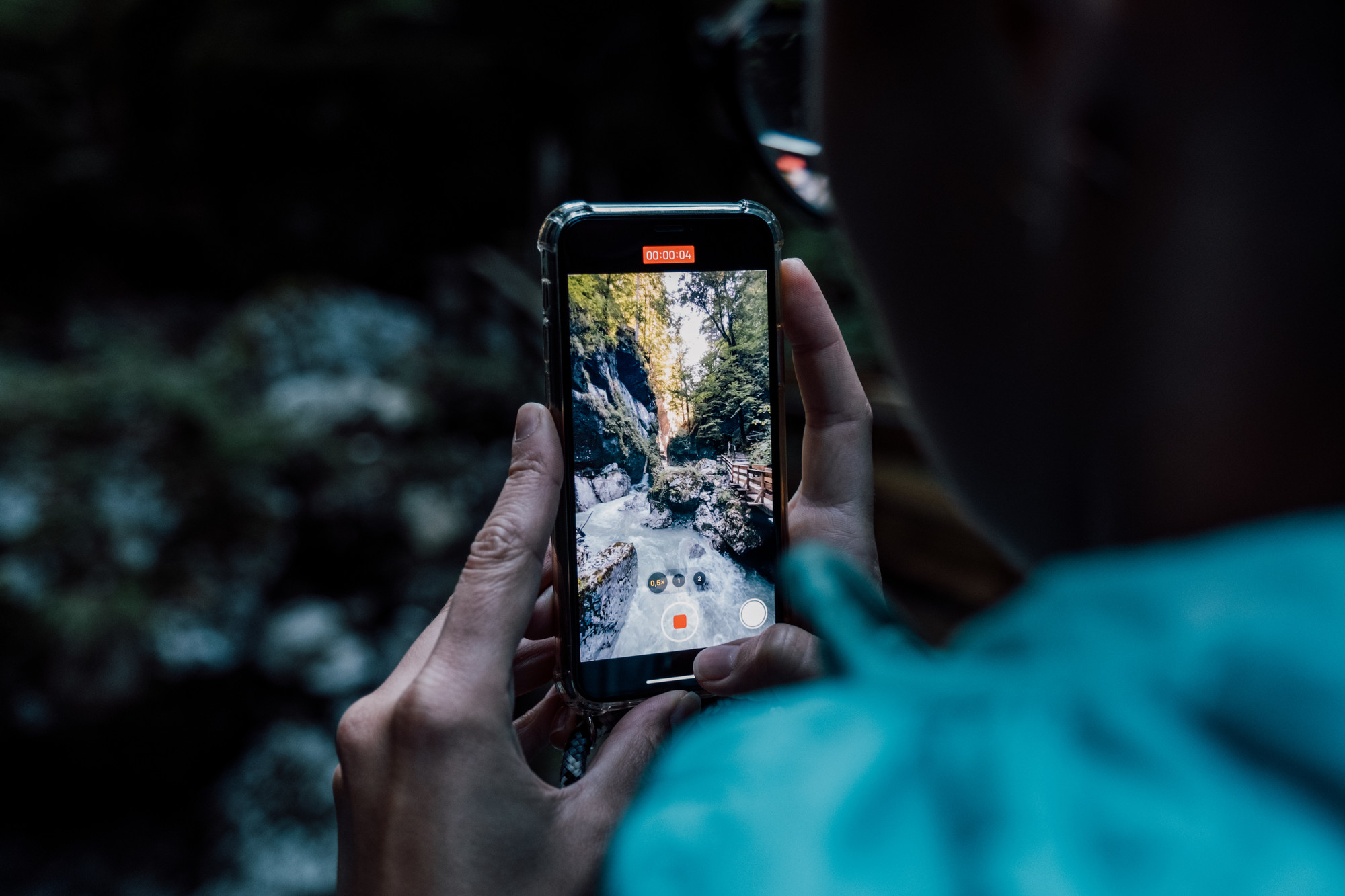 Eine Person fotografiert eine Wald- und Flussszene mit einem Smartphone in beiden Händen.