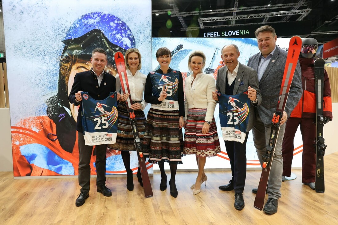 Sechs Personen posieren mit Skilätzchen und Skiern vor einer Skikulisse bei einer Indoor-Veranstaltung.