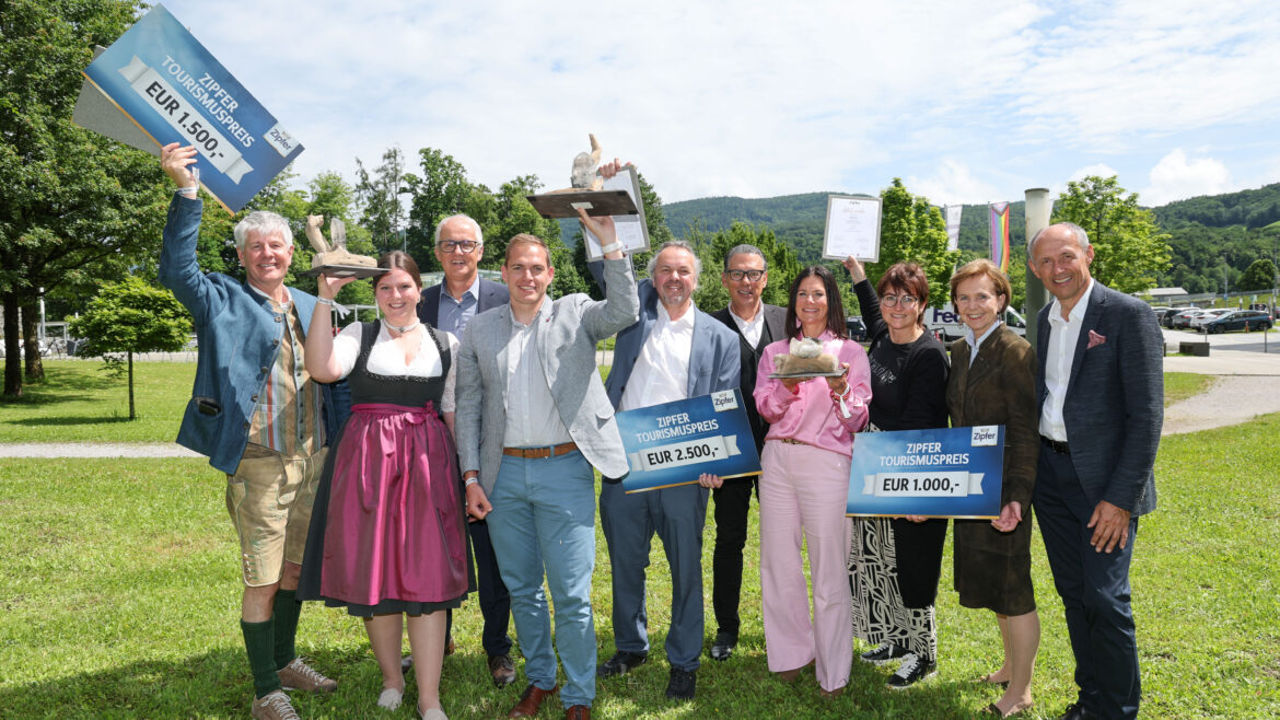 Eine Gruppe lächelnder Menschen im Freien, die Preisschilder und Trophäen halten und an einem sonnigen Tag feiern.