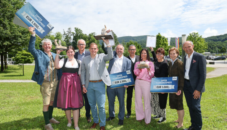 Eine Gruppe lächelnder Menschen im Freien, die Preisschilder und Trophäen halten und an einem sonnigen Tag feiern.