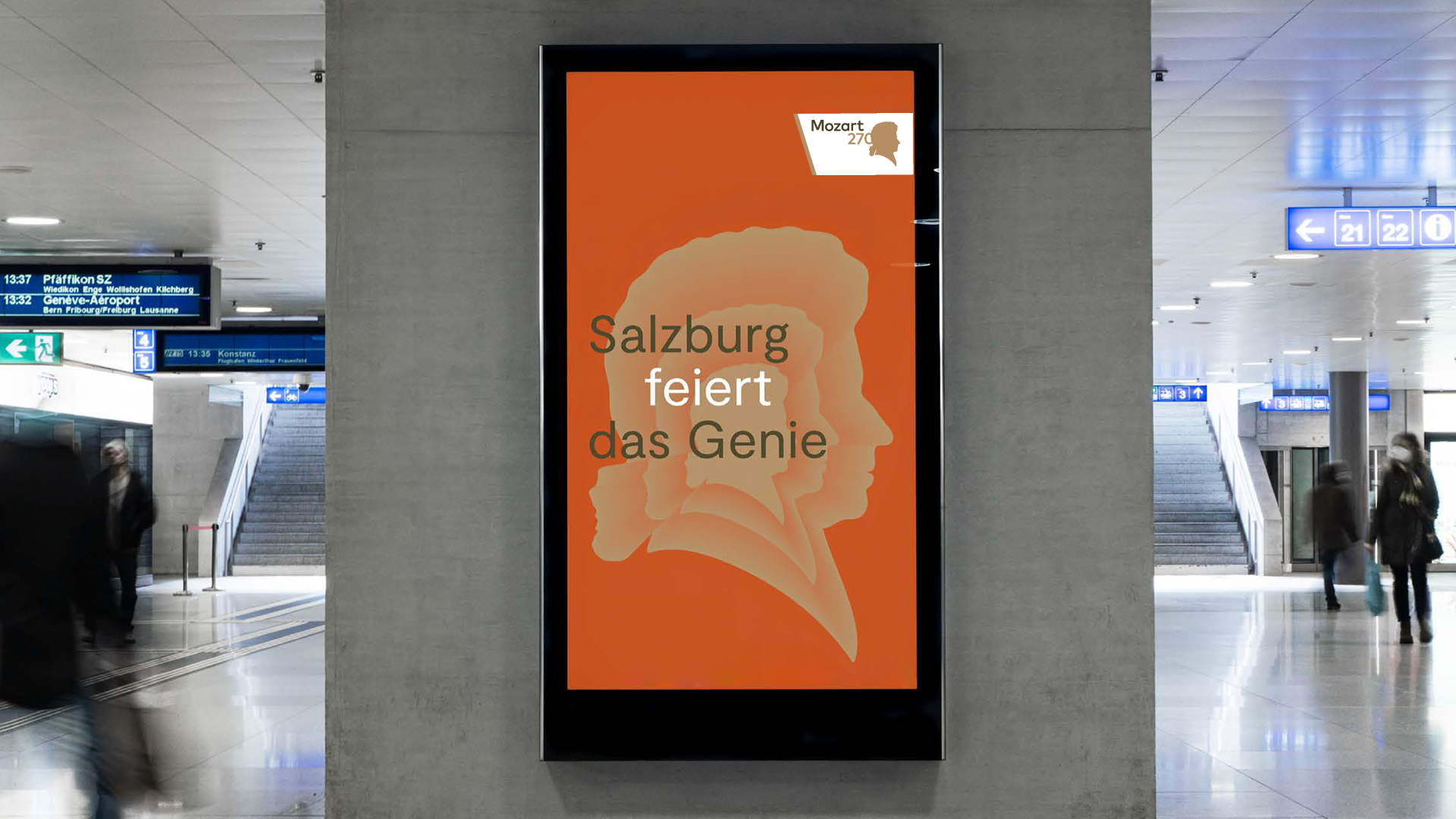 Digitales Plakat in einem Bahnhof mit Mozarts Silhouette und Text: Salzburg feiert das Genie auf orangem Hintergrund.