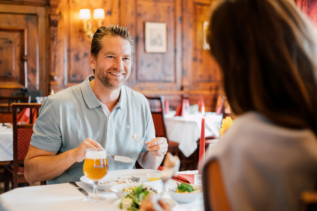 Ein lächelnder Mann genießt eine Mahlzeit mit einer Frau in einem warm beleuchteten, eleganten Speisesaal eines Restaurants.