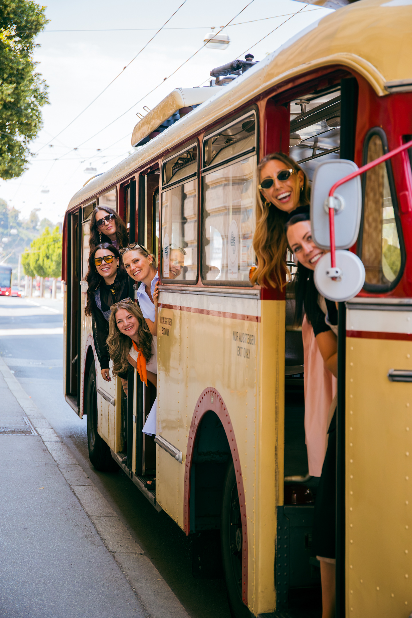 Sechs lächelnde Frauen lehnen sich aus einem gelben Oldtimer-Bus und sind bereit für den „Social Media Sommer 2026“ auf einer sonnigen Straße.