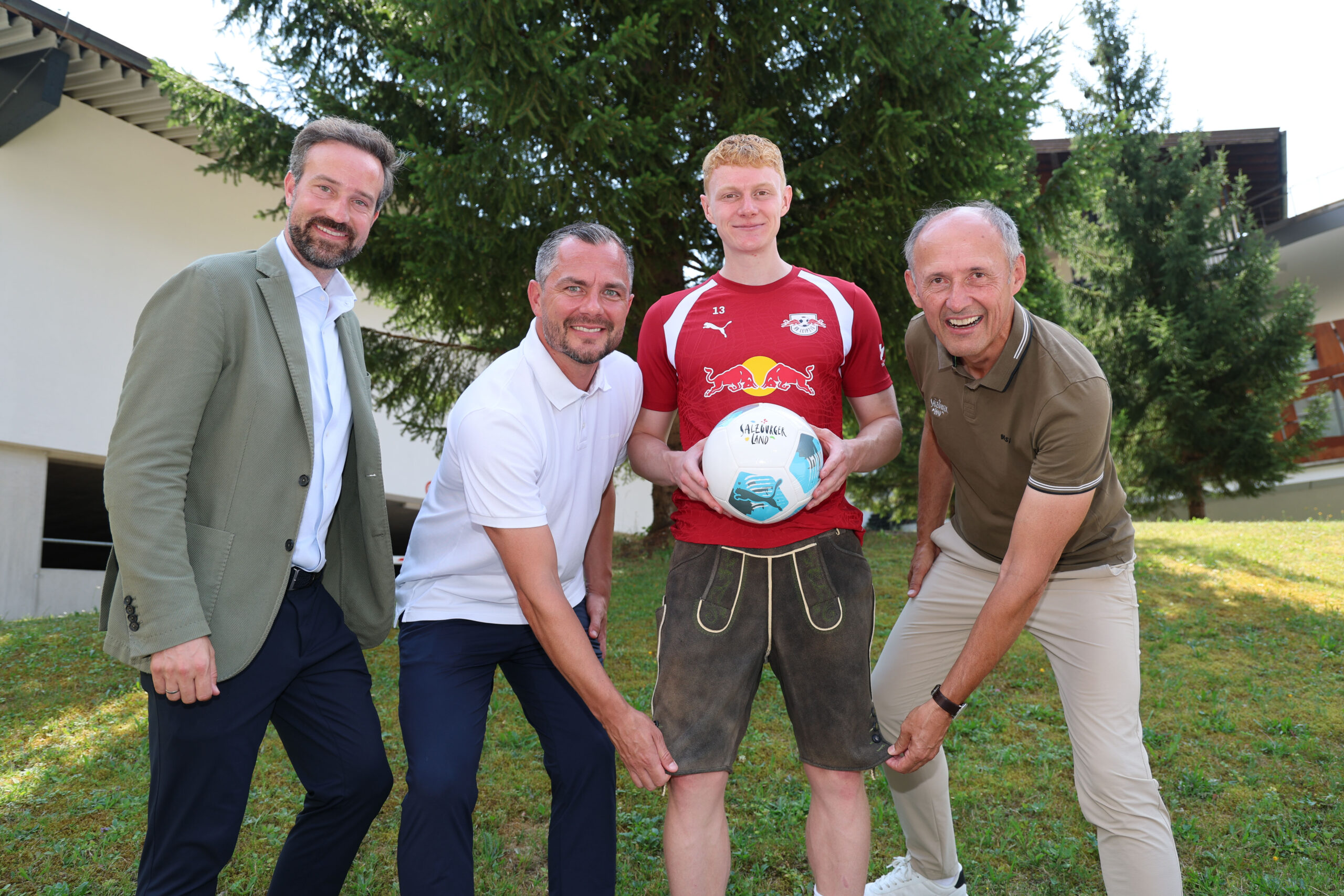 Vier Männer auf einer Wiese beim „1000 Miglia Warm Up Austria 2026“; einer hält einen Fußball in der Hand, alle lächeln.