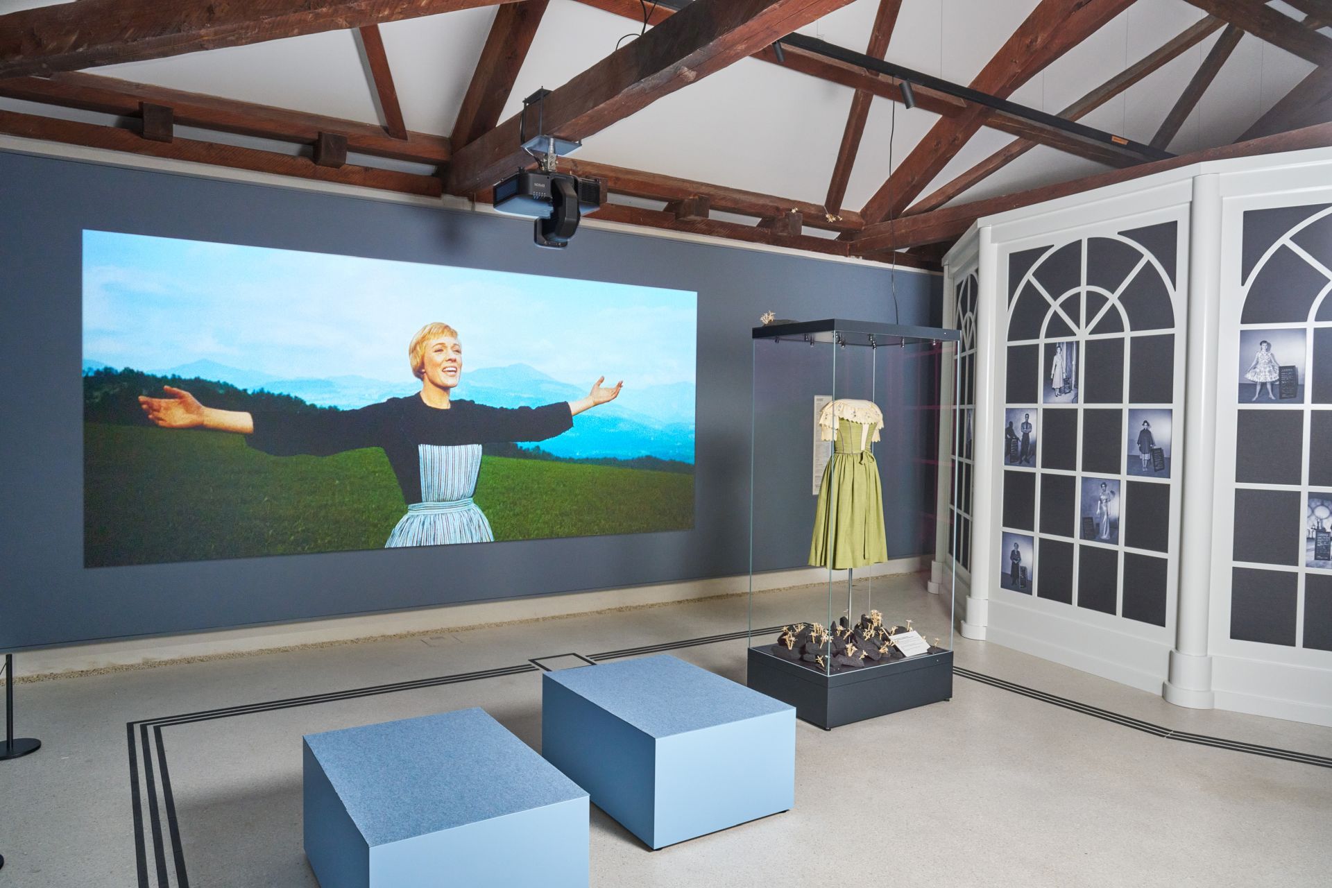 Ausstellung im „Sound of Music“-Museum in Salzburg mit einer singenden Frau, einem grünen Kleid und zwei blauen Bänken.