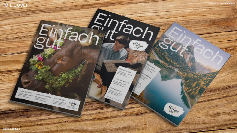 Drei Ausgaben der Zeitschrift „Einfach gut“ auf einem Holztisch, auf deren Titelseiten eine Kuh, ein Koch und ein See abgebildet sind.