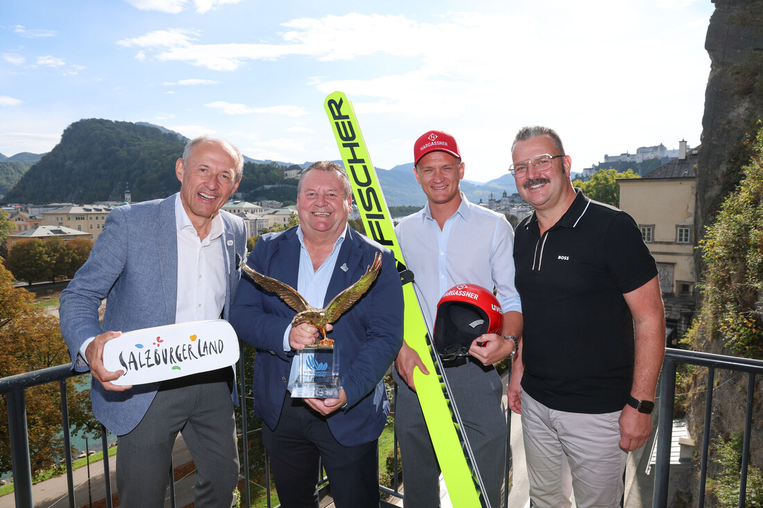 Vier Männer posieren auf einer Terrasse in Salzburg; einer von ihnen hält einen Pokal und ein Paar Skisprungski in der Hand.