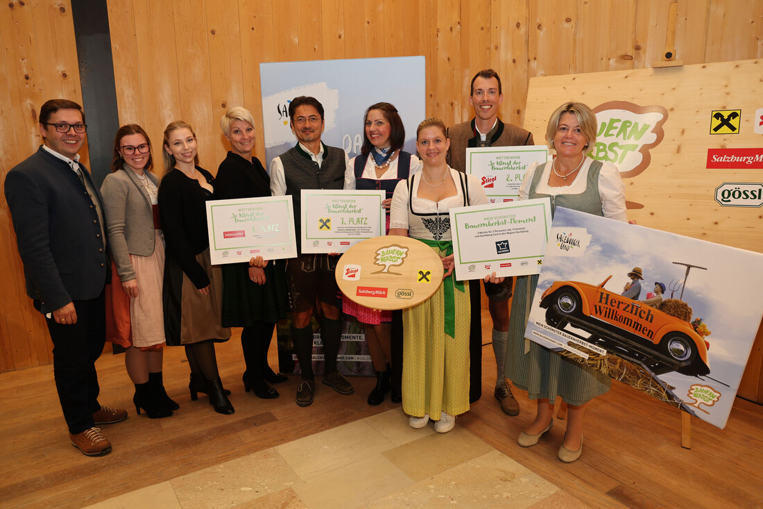 Eine Gruppe von Menschen in österreichischer Tracht, die mit Preisplakaten und einer Holz-Trophäe posieren.